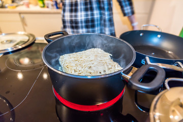 Brick of frozen noodles placed inside pan casserole with boiling water on modern electric cooker