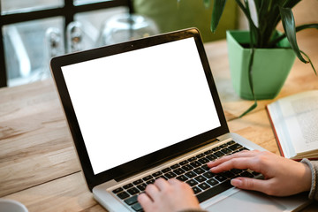 Cropped view of young office worker sitting at table and typing on laptop.