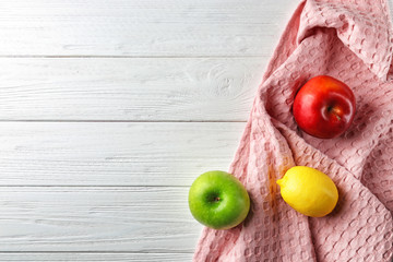 Clean kitchen towel and fruits on white wooden table, top view