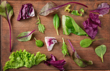 Leaves of different salads on wooden background, top view
