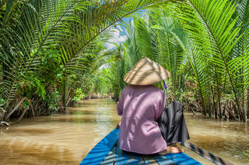Vietnamese woman paddling a traditional boat in the Mekong delta at Ben Tre island. The Mekong river is a major route for transportation in Southeast Asia.