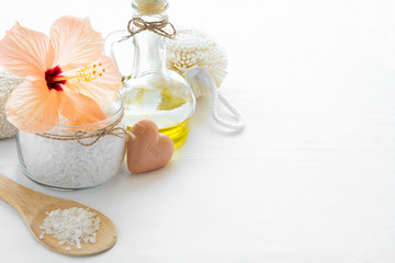 Obraz na płótnie Canvas Wellness setting. Sea salt in glass, soap, towel, olive oil and flowers on white textured background. Space for copy. Flat lay