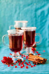 Three glasses of hot mulled wine with pomegranate seeds and spices on turquoise background