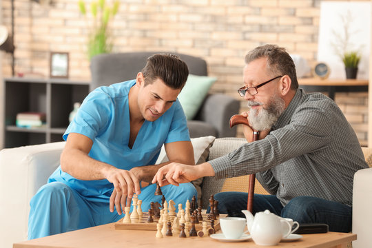 Young caregiver and senior man playing chess at home