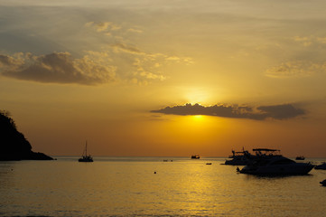 amazing tropical orange sunset over water, with rock silhouettes and a boat on Phuket Island, Thailand