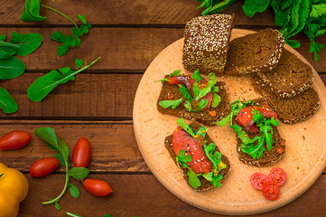 Bruschetta with salmon, red fish, red caviar, arugula and tomatoes on a board. Wooden rustic background. Selective focus. Top view