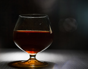 Glass of brandy or cognac on the old dark wooden background with copy space