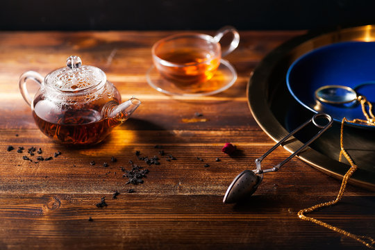 Picture of glass teapot with cup of black tea and golden tray on wooden table. Overhead view, copy space.