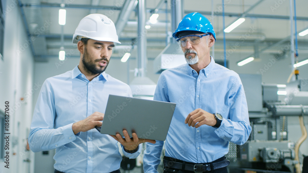 Poster head of the project holds laptop and discusses product details with chief engineer while they walk t
