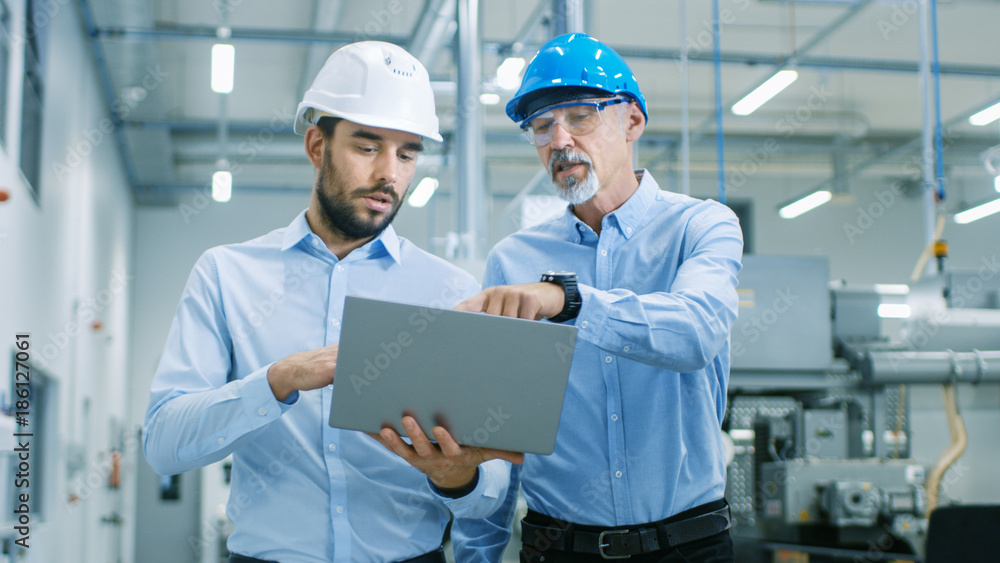 Poster head of the project holds laptop and discusses product details with chief engineer while they walk t