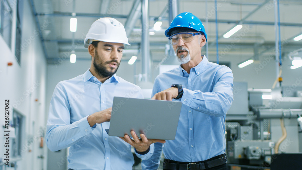 Poster head of the project holds laptop and discusses product details with chief engineer while they walk t