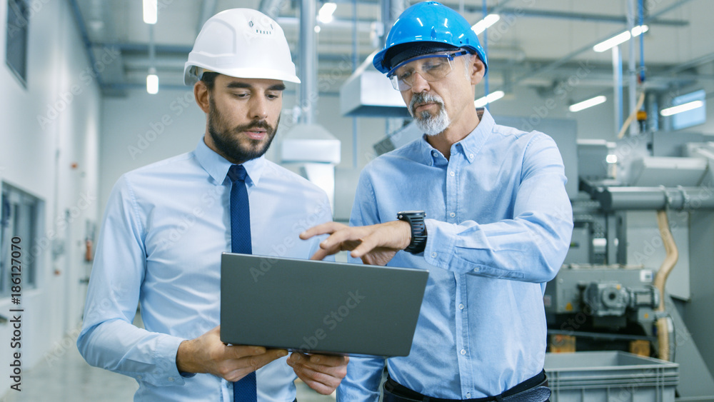 Poster head of the project holds laptop and discusses product details with chief engineer while they walk t