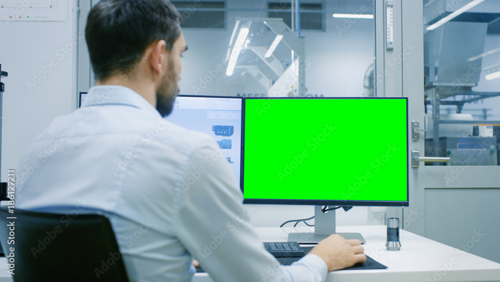 Poster engineer/ technician working on a personal computer with two displays, one has a green screen chroma