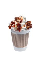 coffee in a paper cup with whipped cream, chunks of chocolate and caramel topping on a white background