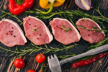 Beef steak with fresh vegetables and rosemary and spices on a black wooden background. Top view. Free space for text.
