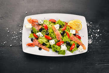 Salmon salad, feta cheese, salad leaves and fresh vegetables on the plate. On a wooden background. Top view. Free space for text.