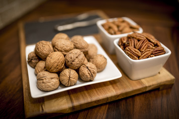 A healthy and nutritious selection of nuts on a wooden serving board with walnuts, pecans, and almonds in contemporary white bowl and plates