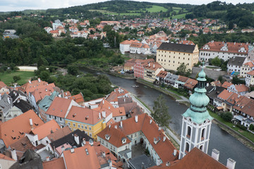 Fototapeta na wymiar View of the charming medieval town, Cesky Krumlov, from the castle tower. Looking over the town from high up, Church of St Jost overlooking the Vltava River flowing through the town green hills beyond