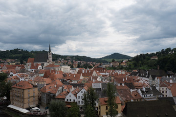 Fototapeta premium View of the charming medieval town, Cesky Krumlov, from the castle. St Vitus Church and the town of Cesky Krumlov, green mountains and stormy sky. Red roofed houses in charming town in Europe.