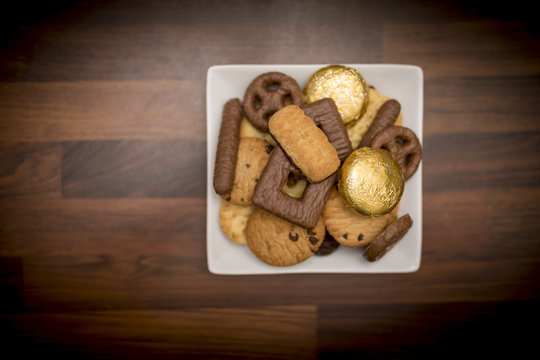 Delicious, Yummy And Luxurious Plate Of Luxury Biscuits Including Chocolate Chip Shortbread Cookies, Chocolate Digestives And Orange Creme Biscuits Shot From Above On A Butchers Block Worktop