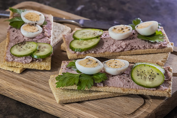 Fresh homemade meat pate on over crispbread on wooden board. Soft focus.