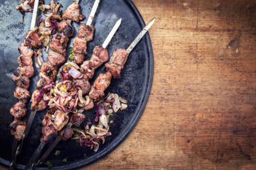 Traditional Russian shashlik on a barbecue skewer with roasted onion as top view on cutting board with copy space right