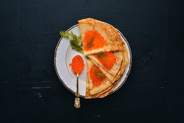 Pancakes with red caviar on a plate. On a wooden background. Top view. Free space for text.