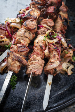 Traditional Russian shashlik on a barbecue skewer with roasted onion as top view on board