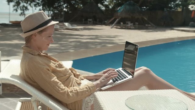 Portrait of a young woman using laptop computer. Woman working with computer on vacation in luxury resort.
