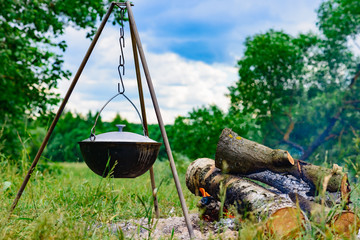 a camp-steaky sooty food bowl hanging on a tripod over a fire