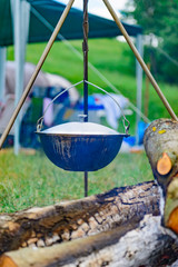 a camp-steaky sooty food bowl hanging on a tripod over a fire