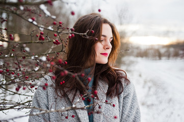 Close up portrait of gentle girl in gray coat near the branches of a snow-covered tree.