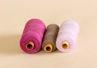 Three skeins of thread lay on a beige background. Purple, lilac and gray fine yarn. Articles for sewing and needlework. Horizontal image.