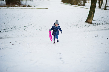 Cute little girl with saucer sleds outdoors on winter day.