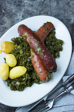 Gr&uuml;nkohl mit Pinkel und Gr&uuml;tzwurst auf einerm Teller mit Kartoffeln und Besteck