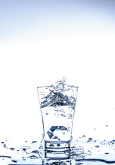 Ice dropping and water splashing in the glass with reflection on the mirror table and isolated on white background.