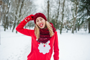 Fototapeta na wymiar Blonde girl in red scarf, hat and santas sweater posing at park on winter day.