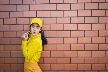 Portrait asian hipster girl on brick wall background,she wear yellow tone full body,Lifestyle of thailand people