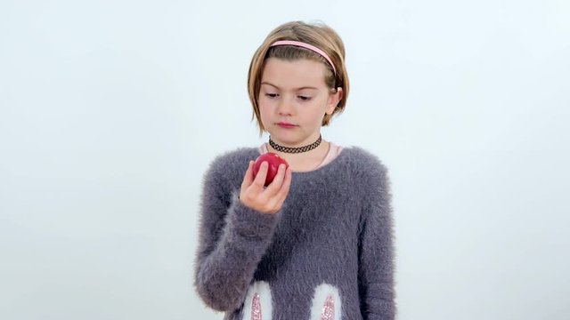 A young girl is tasting a red apple and she doesn't like it very much.
