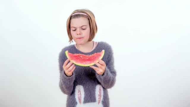 A pupil is eating a slice of watermelon for her snack.