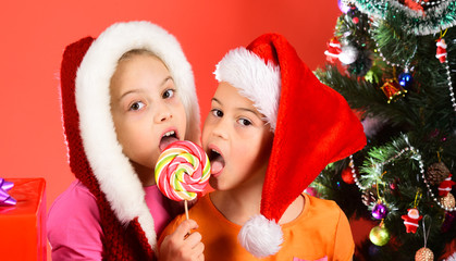 Children with happy faces share lollipop on red background.