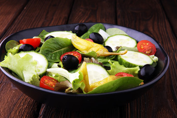 bowl of salad with vegetables and greens, with tomato, cucumber and onions.