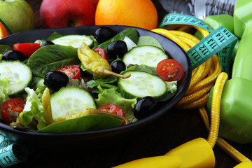 Fitness concept with salad bowl, dumbbells, skipping rope, bottle water, apples and tape measure