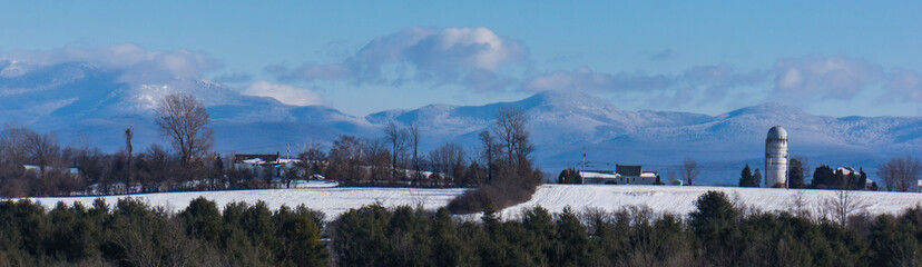 banner panorama view of the Green Mountains of Vermont USA in winter with snow, a farm with silo in foreground 
