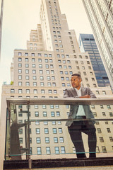 Modern City Life. African American Businessman working in New York. Young black man standing by railing in business district with high buildings, looking around, seriously thinking - tough work ahead