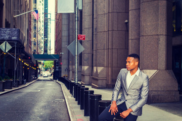 Naklejka na ściany i meble African American Businessman working, traveling in New York. A college student sitting on metal pillar on street, outside office building, thinking. Small car running on background. Filtered effect..