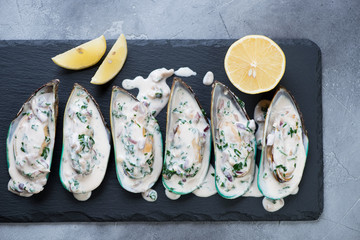 Kiwi mussels with cheese sauce and lemon on a stone slate, horizontal shot, top view