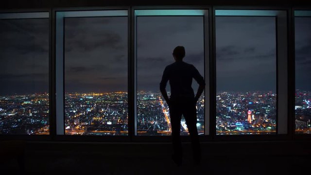Man looking out large windows high above a sprawling city