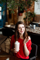 The girl with blue eyes in a red dress drinks nonalcoholic milkshake in cafe.