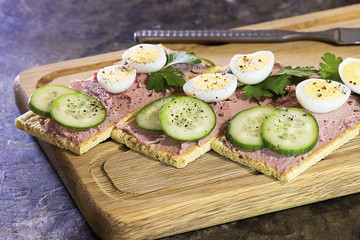 Fresh homemade meat pate on over crispbread on wooden board.